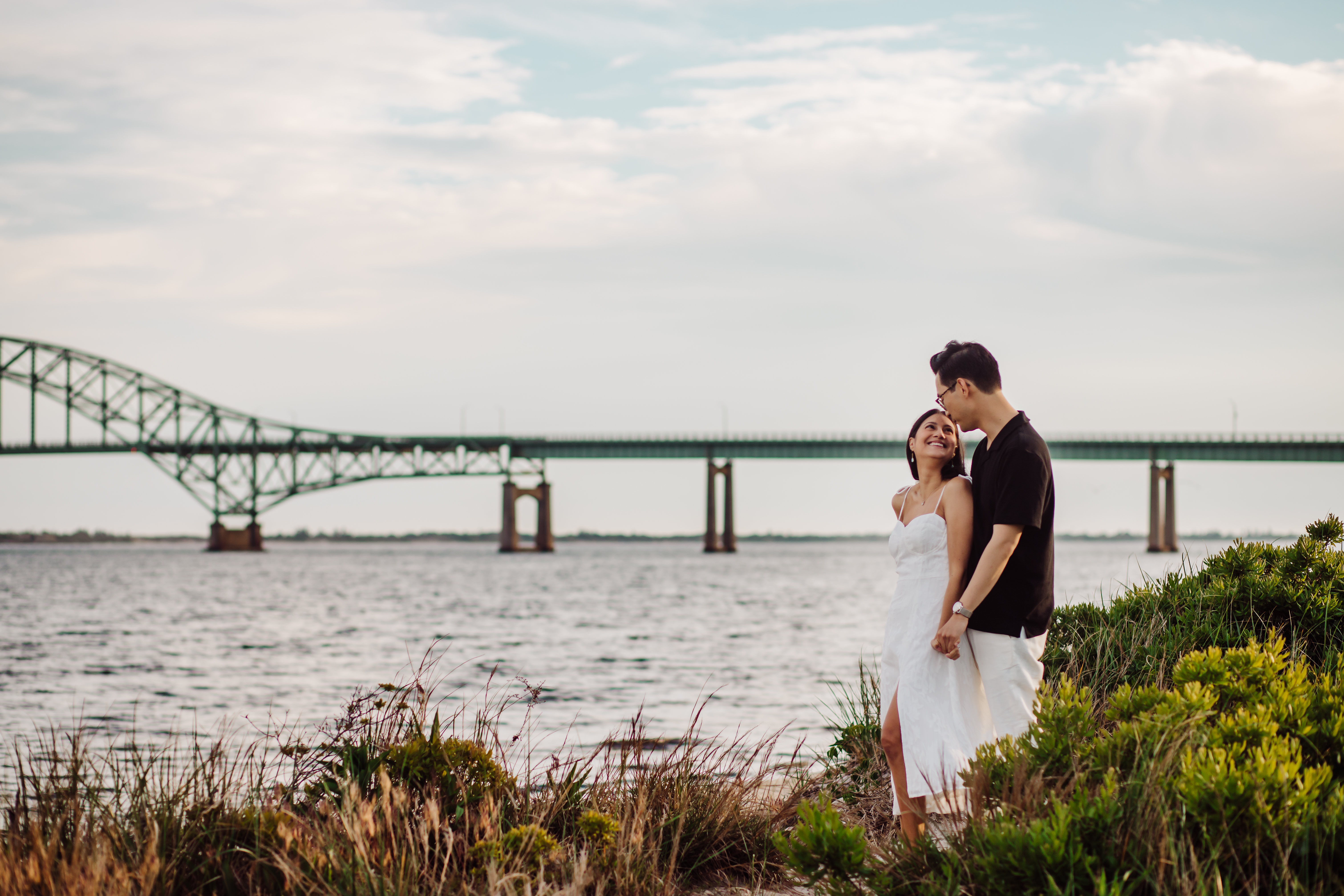 Chris and Angela's engagement session at Captree State Park during golden hour, with the couple sharing a loving moment in front of the iconic bridge.